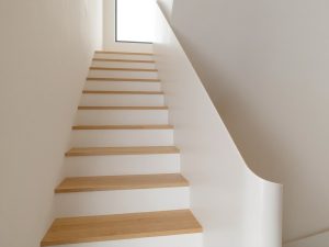 Treppe mit hellen Holzstufen und foliert wirkenden, matt weißen Setzstufen und Wangen, digital erzeugte Darstellung