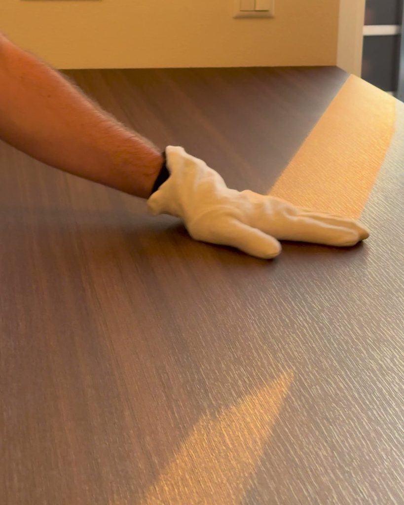 Hand im Handschuh streicht über eine folierte Arbeitsplatte im Gegenlicht